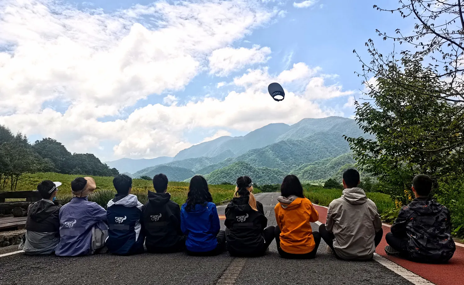 九名队员背对镜头坐在山间公路边