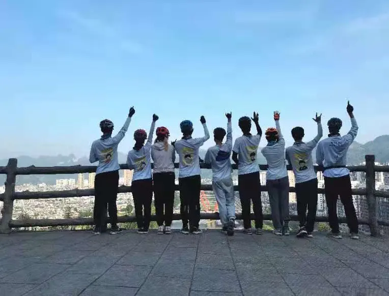 九名队员背对镜头站在观景台栏杆前举手