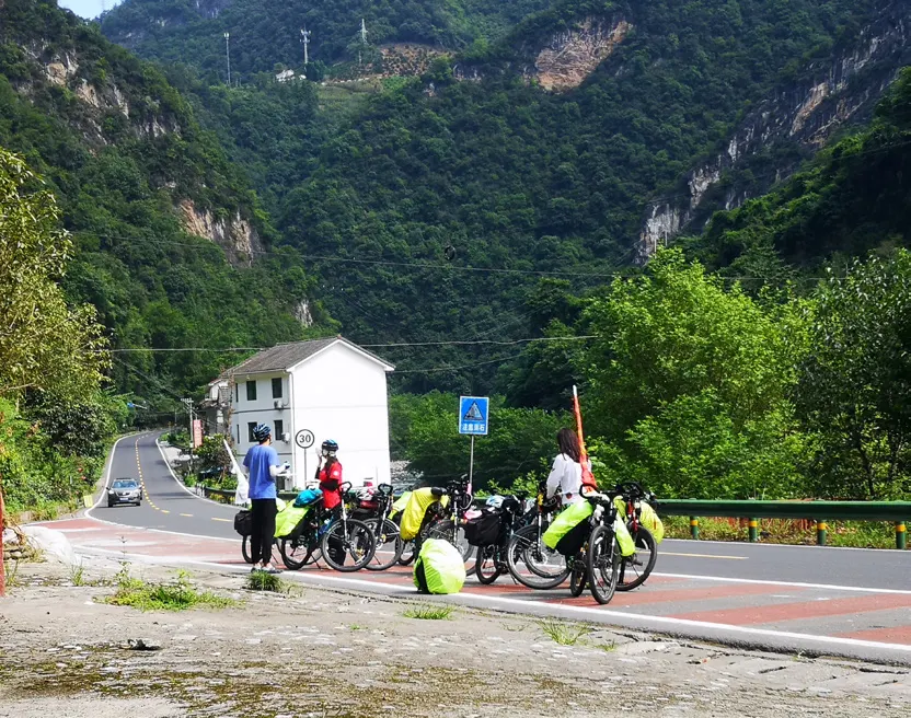队员们和自行车停在峡谷公路边的白房子前