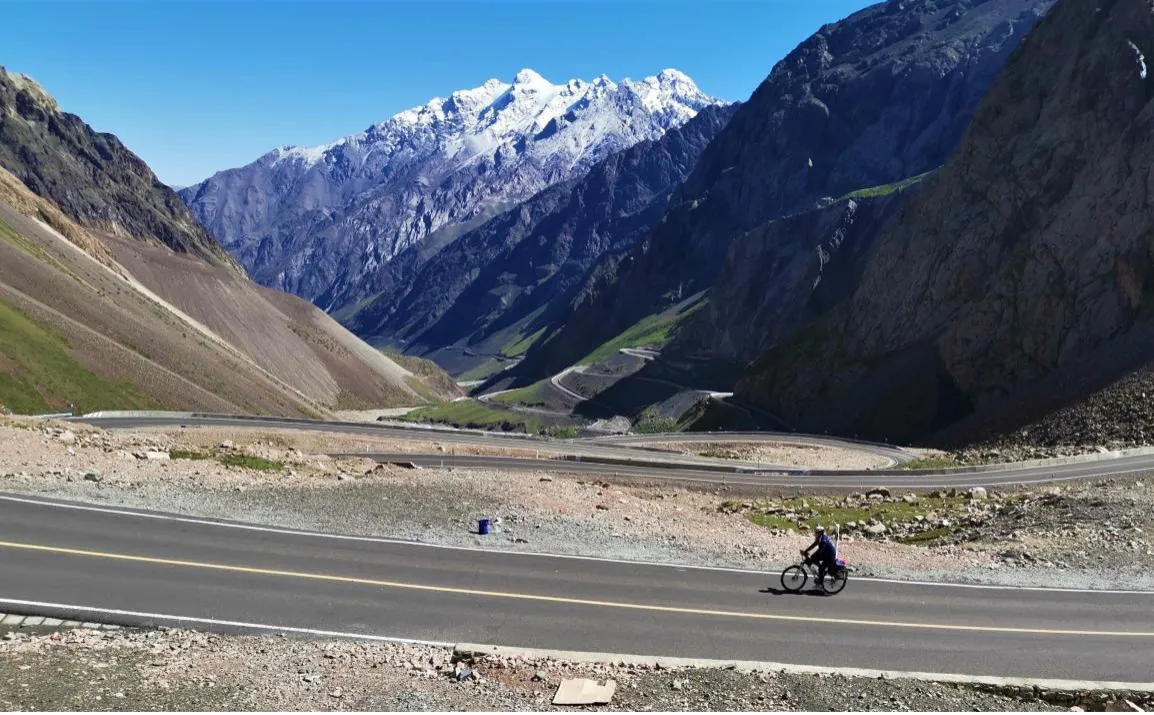 雪山下的独库公路，一名骑行者驶过盘山路